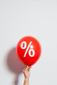 A red balloon with a percentage symbol held against a white background, symbolizing discounts and sales.