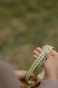 Close-up of hands holding a measuring tape outdoors, displaying various measurements.